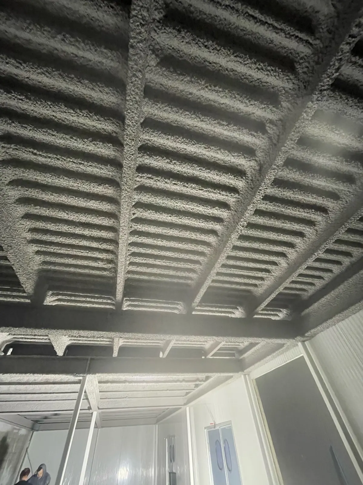 Grey cementitious fireproofing sprayed on steel joists and deck in a commercial building
