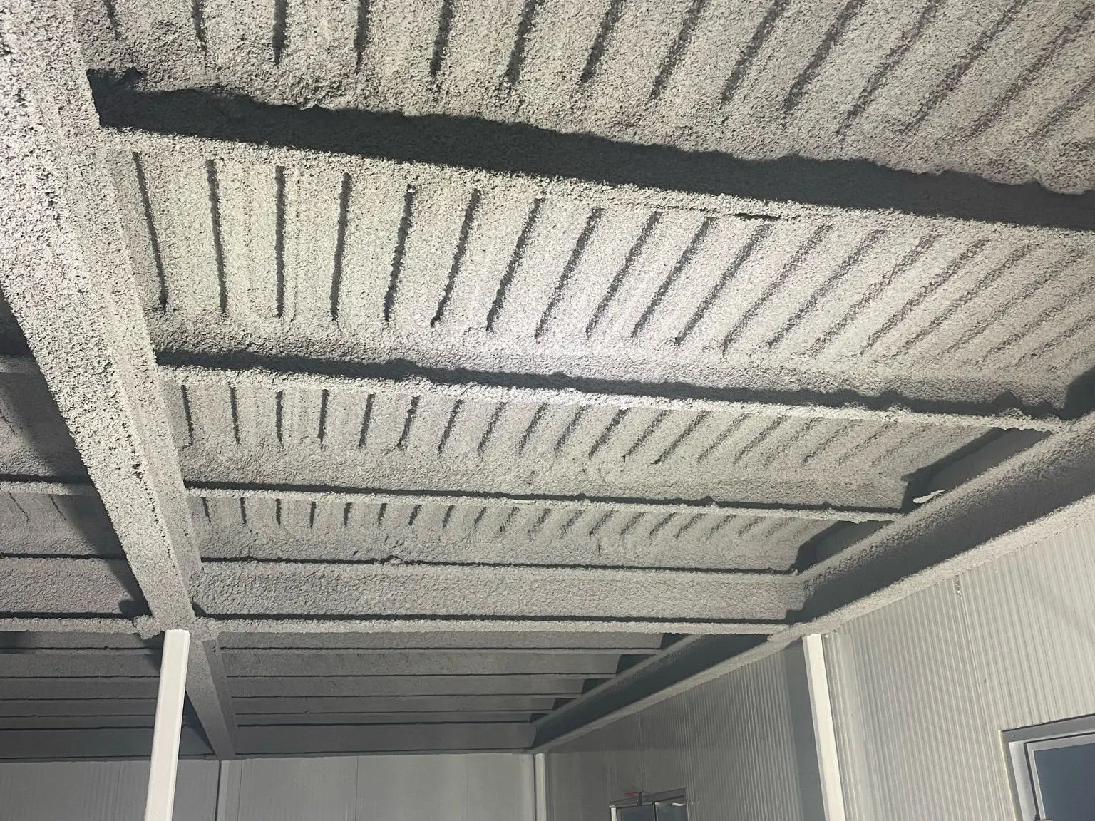 Steel beams and corrugated deck ceiling covered in grey cementitious fireproofing