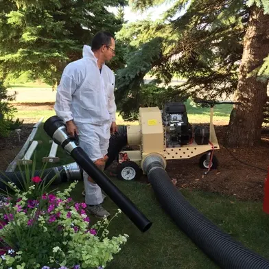 Aires worker in a protective suit beside a portable vacuum unit with large black hoses on a front lawn