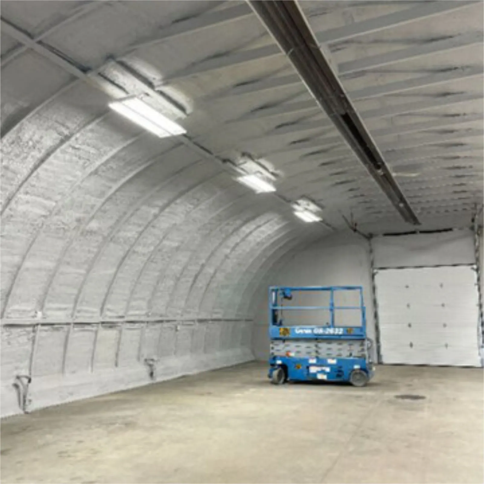 Quonset interior with spray foam coated white in DC315 fireproof paint and a scissor lift on the floor