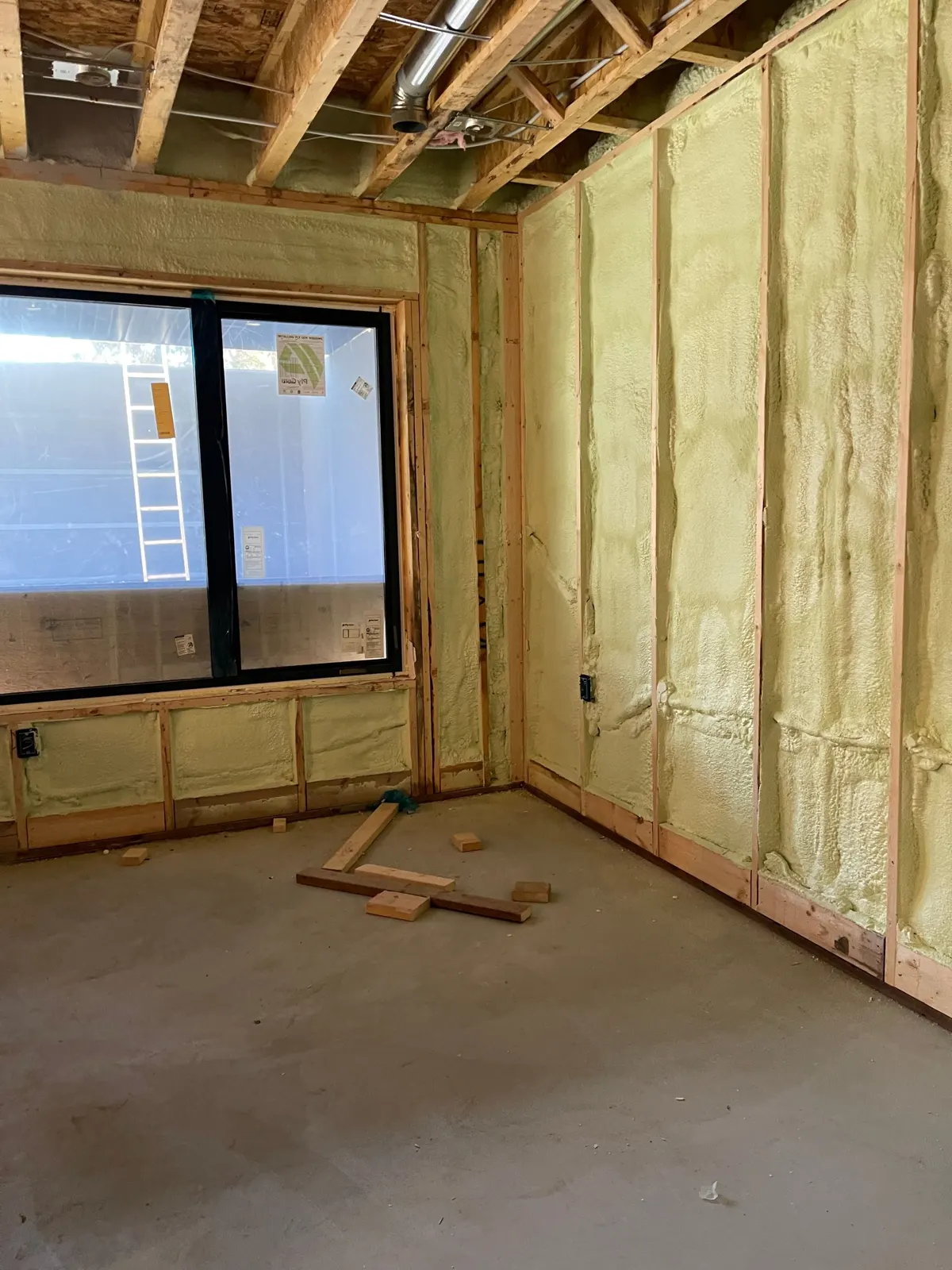 House wall around a window insulated with spray foam between the studs