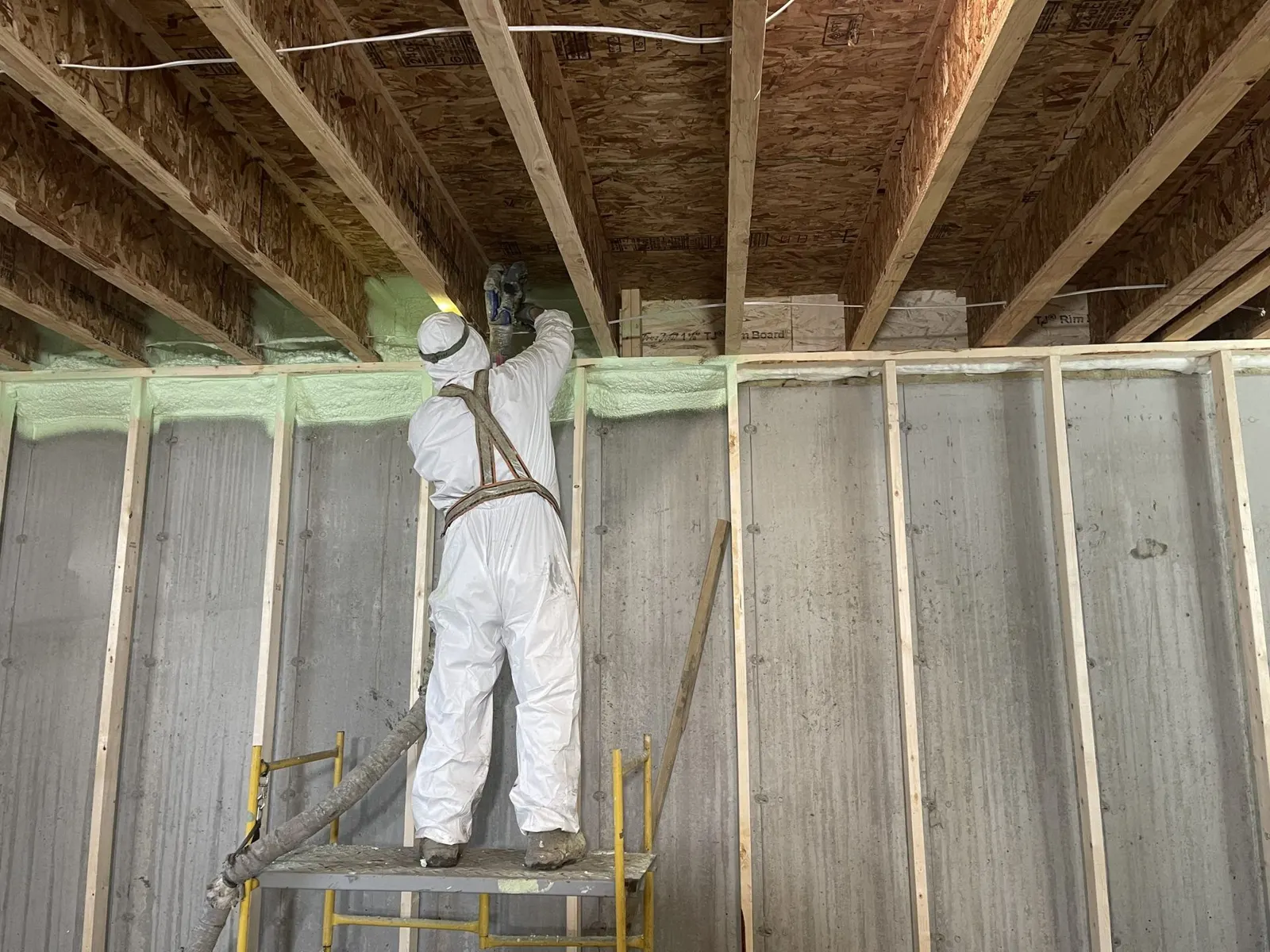 Installer in a protective suit spraying foam on a basement rim joist