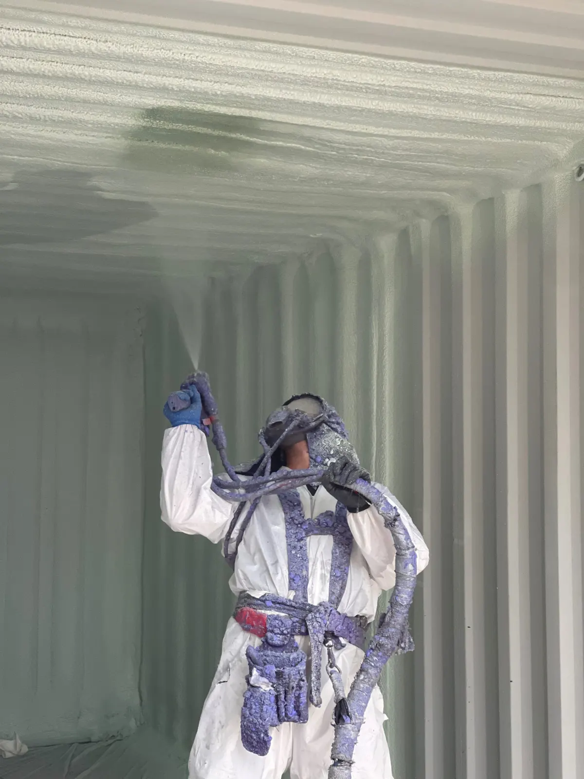 Installer in a protective suit spraying foam on the walls inside a shipping container